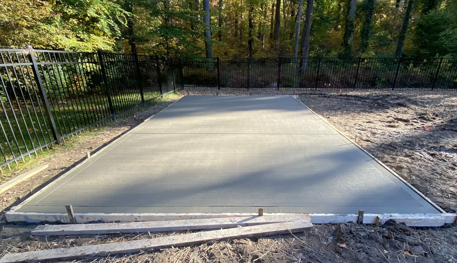 A finished concrete parking pad with cut control joints in a fenced back lot &mdash; Little Acres Grading