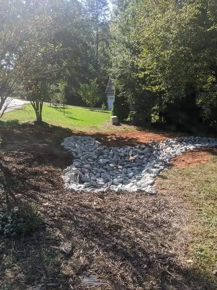 A stone-lined dry creek swale built to carry runoff away from a yard &mdash; Little Acres Grading