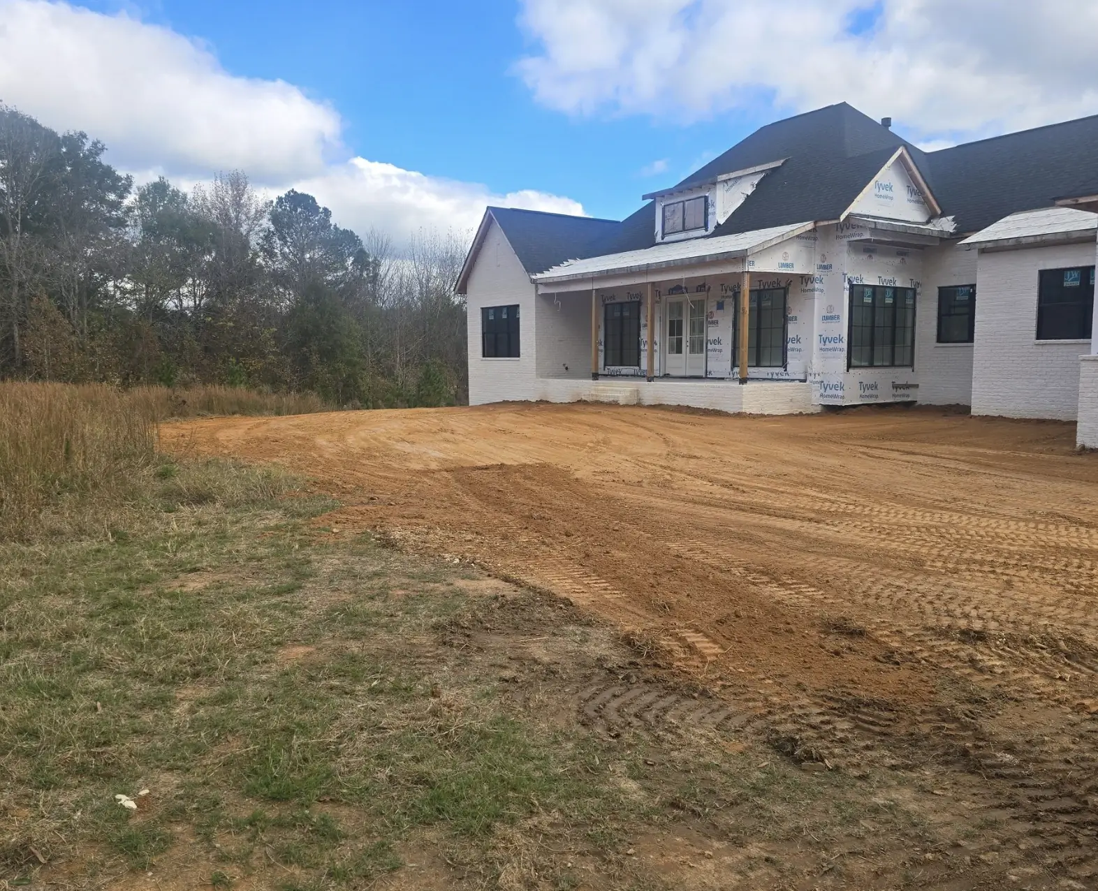 A red-clay yard cut to grade around a white farmhouse under construction &mdash; Little Acres Grading