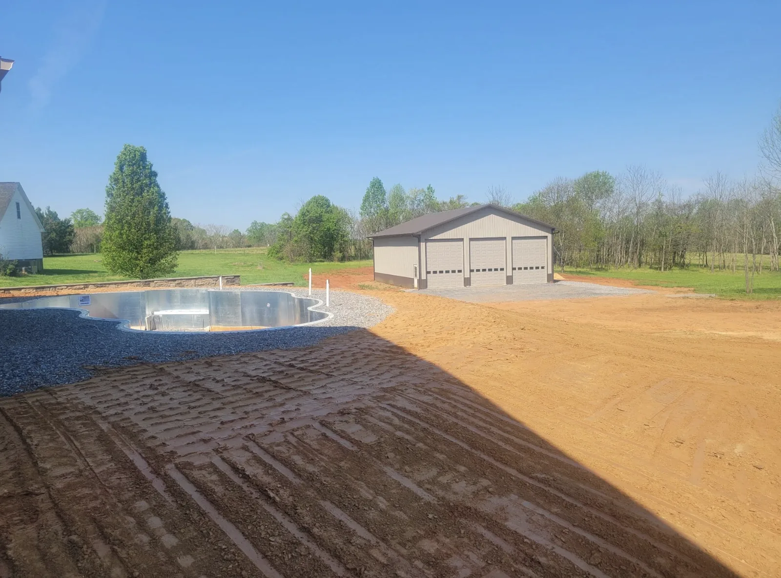 A graded yard and stone pool surround beside a newly built shop building &mdash; Little Acres Grading