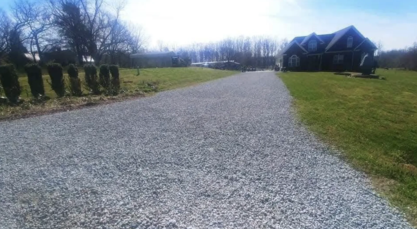 A wide gravel driveway running up to a stone-front home in winter &mdash; Little Acres Grading