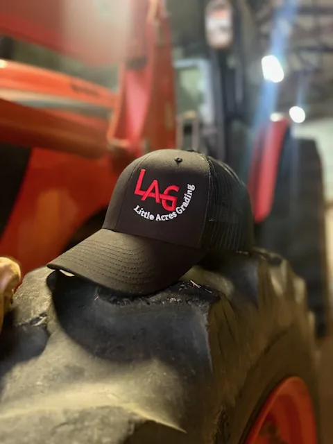A Little Acres Grading cap resting on a tractor tyre &mdash; Little Acres Grading