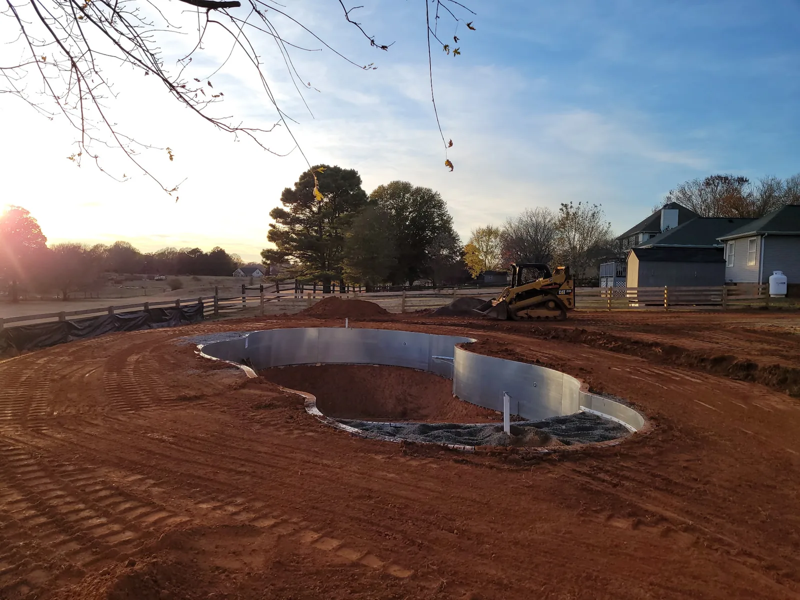 A freeform pool excavation with a skid steer working the backfill at sunset &mdash; Little Acres Grading