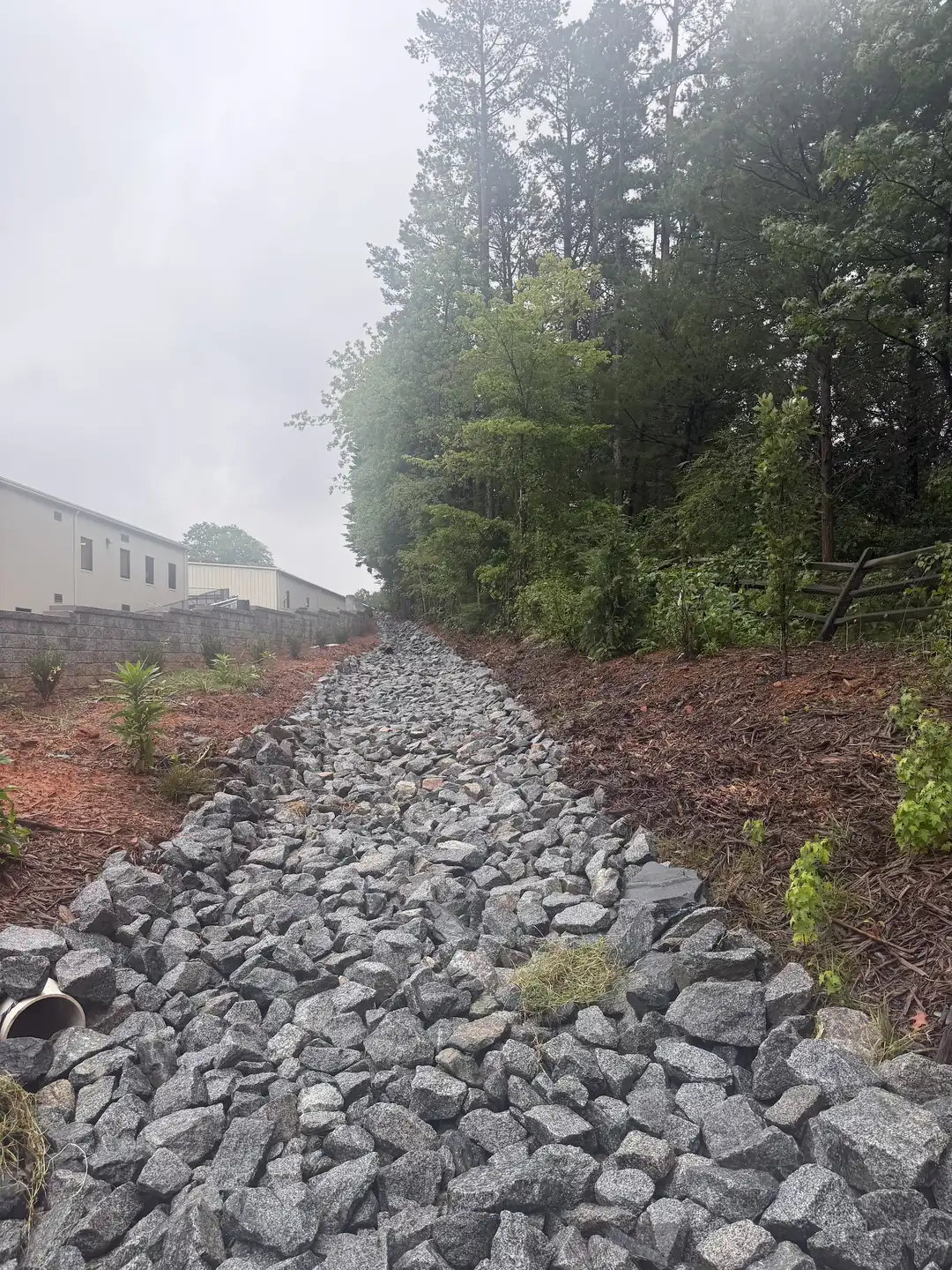 A rip-rap drainage channel cut behind a commercial building &mdash; Little Acres Grading
