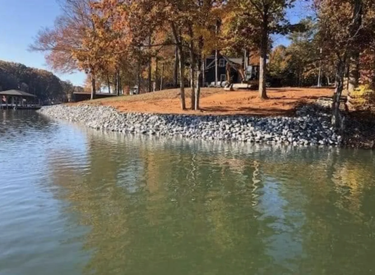 Rip-rap along a lake shoreline below a house in autumn colour &mdash; Little Acres Grading