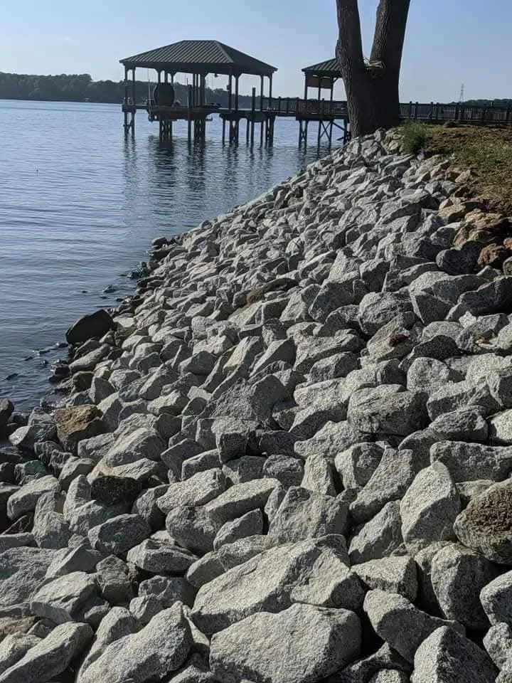 A stone shoreline armored with rip-rap beside a private boat dock &mdash; Little Acres Grading