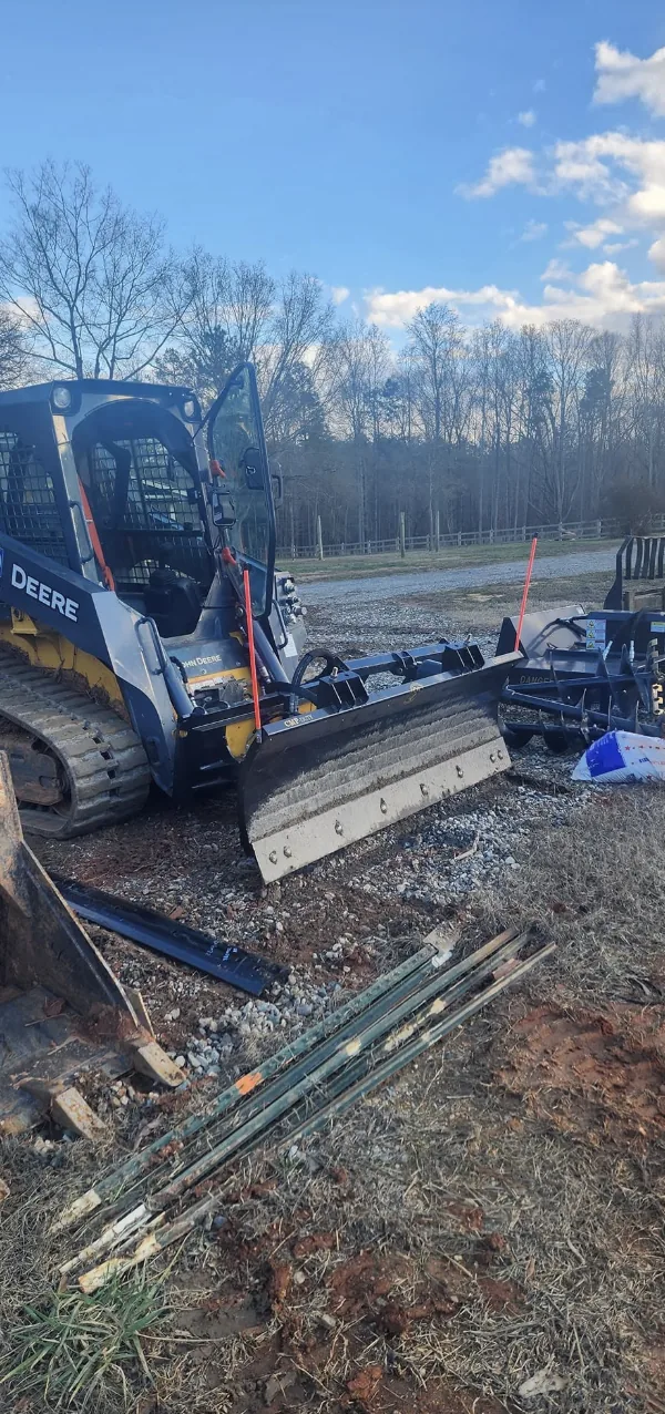 A skid steer fitted with a grading blade on a winter job site &mdash; Little Acres Grading