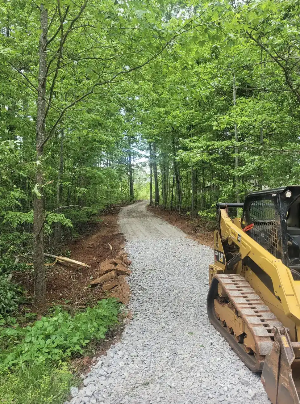 A skid steer alongside a newly cut gravel road through the woods &mdash; Little Acres Grading